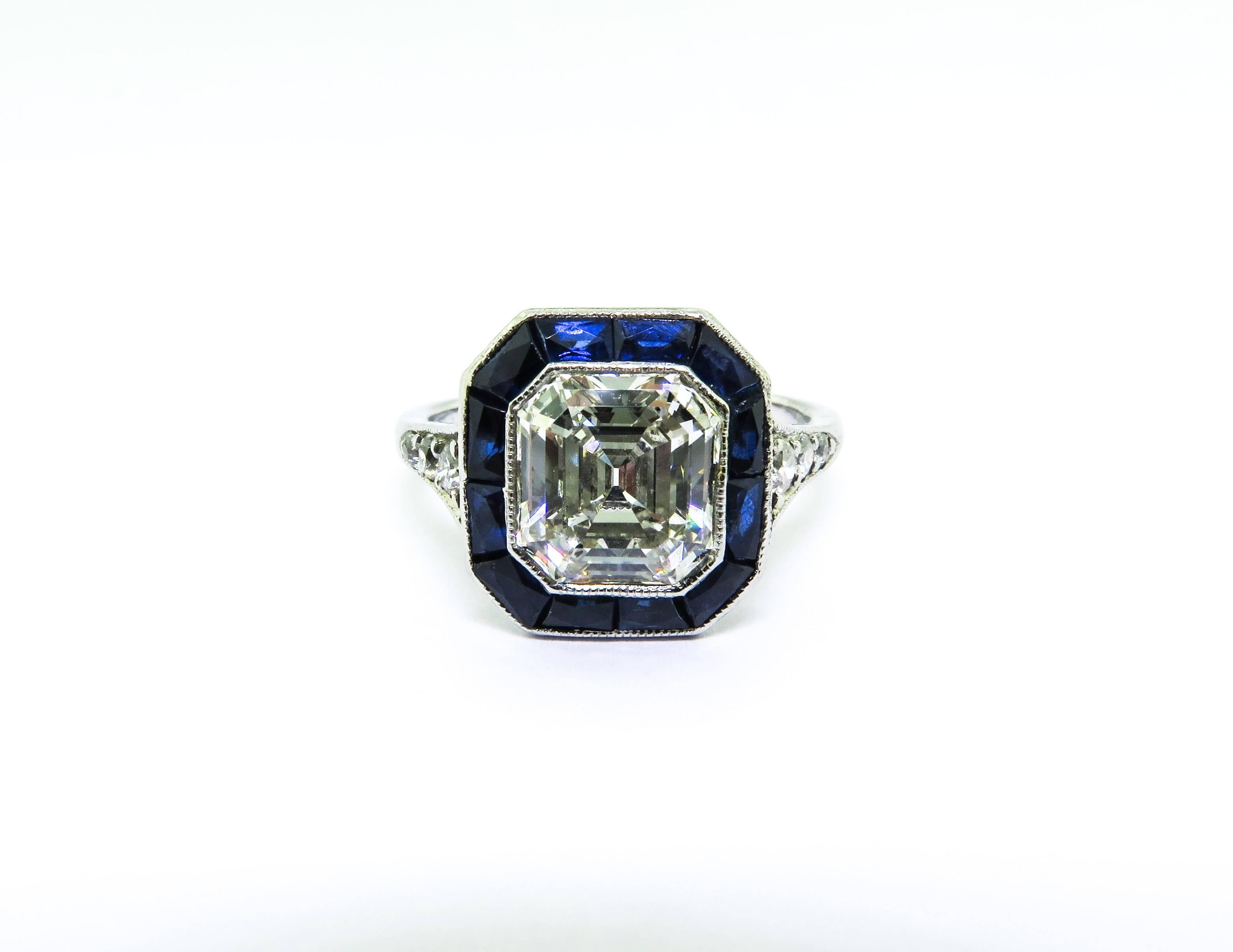 This modified emerald cut (asscher) diamond ring with baguette cut sapphire halo bezel set with beaded edge. With diamond details, and craftsmanship from around the 1920's. The 2.20 ct. center diamond is H color and SI1 clarity. This would make the