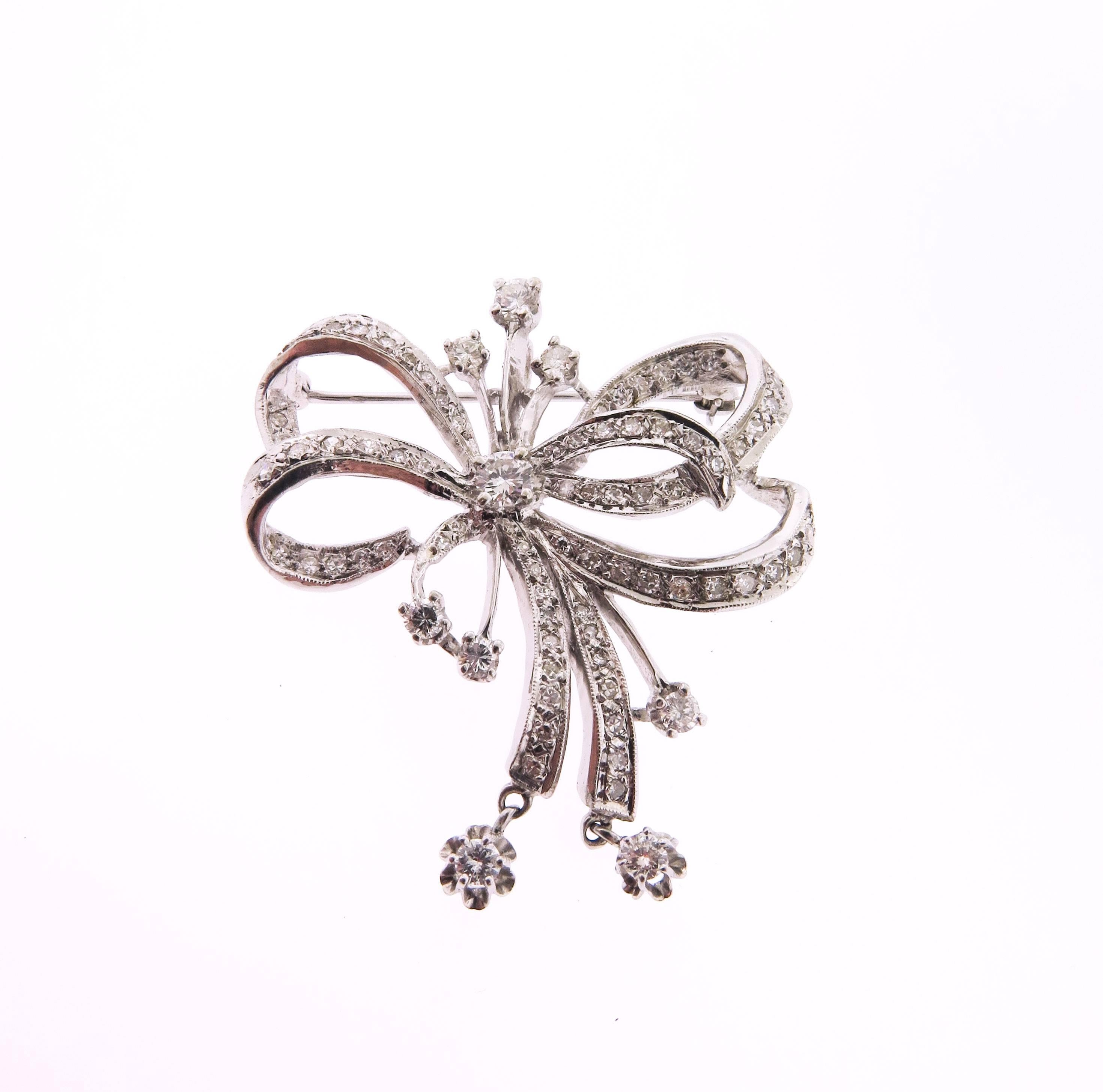 Antique brooch in the form of an openwork bow that is covered with round cut diamonds and boasts a claw set diamond drops. The brooch features a pin clasp as well as a hidden baile that enables you to wear it as a pendant. 
