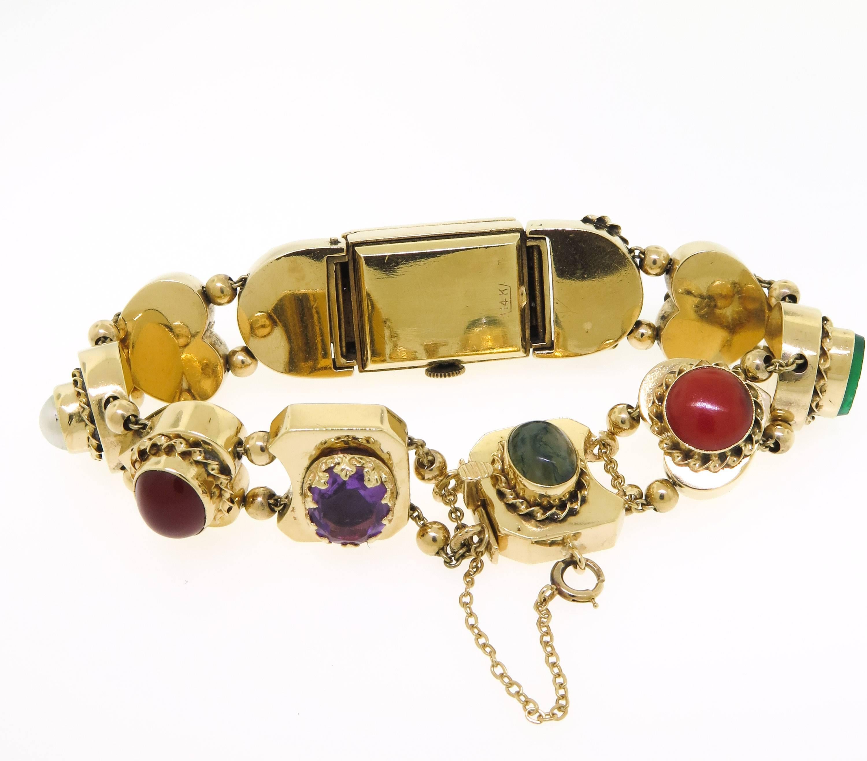 This vintage bracelet features 10 charms in different shapes and colored stones set in 14K yellow gold. This piece measures 7 inches with a box clasp closure and safety chain; the largest charm at the center features a hidden rectangular shaped