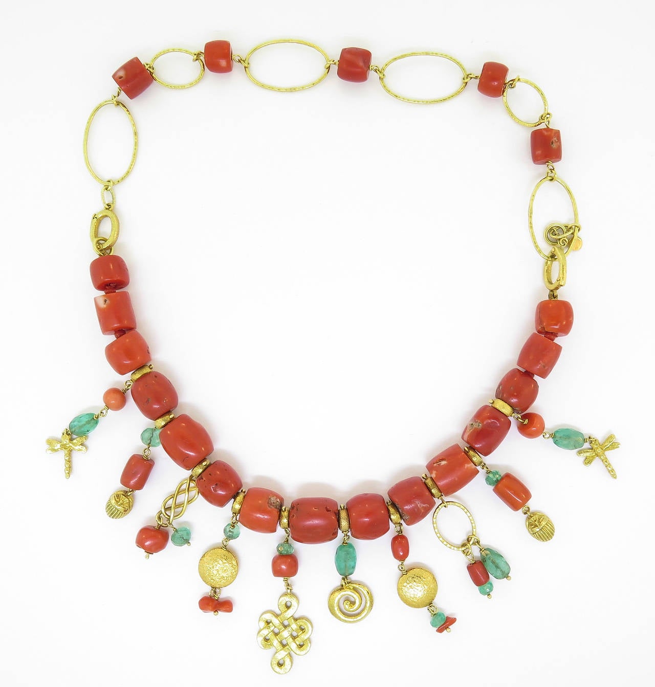 This whimsical necklace is handcrafted in 18K yellow gold featuring vintage coral and emerald beads.  The charms are inspired by the makers findings at numerous markets from the far corners of the world! It can also be worn as a bracelet.