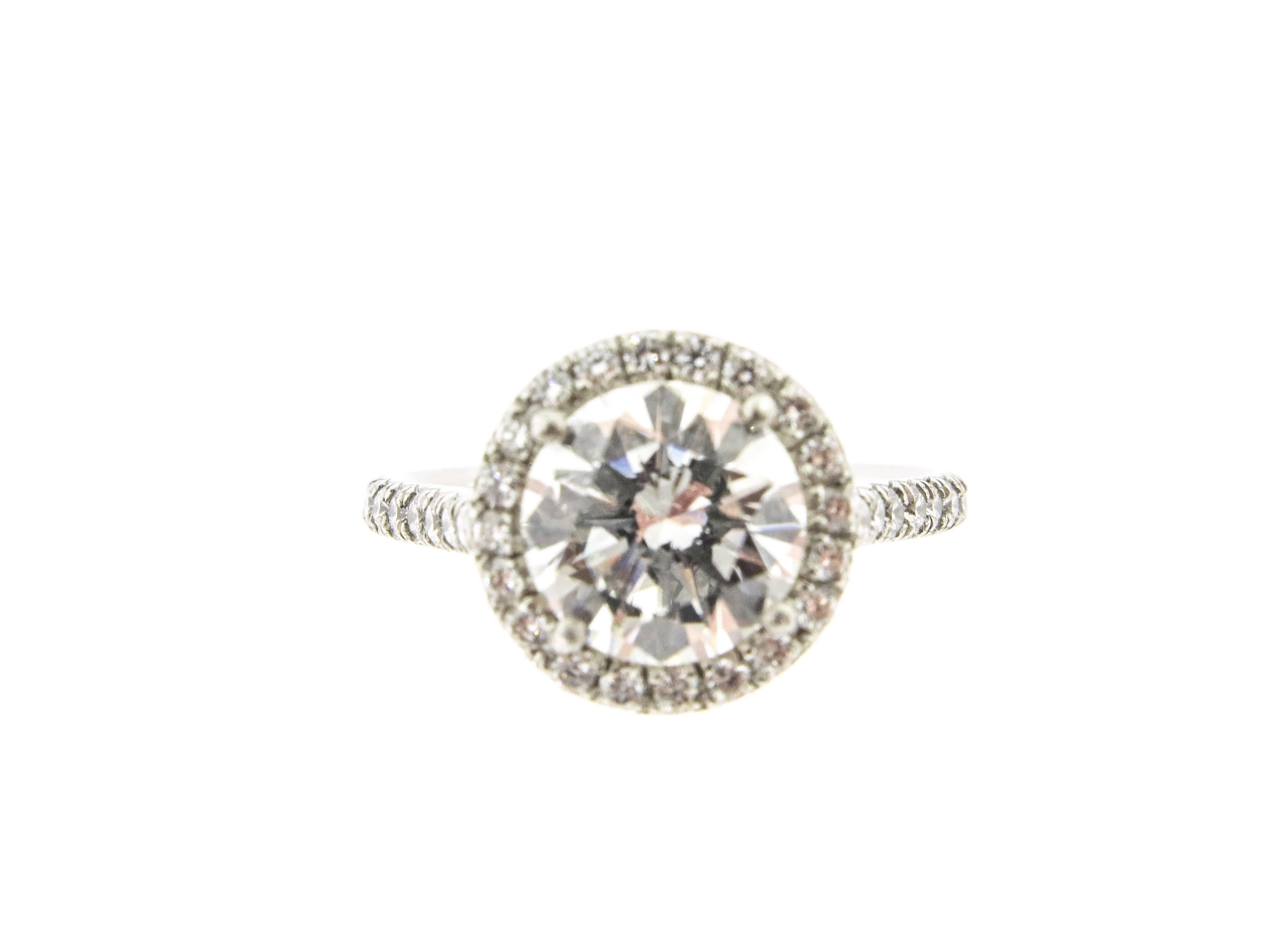 The craftsmenship is oustanding!  Surrounding a round cut diamond with exquisite bead-set diamonds that cast a halo of sparkling light. The center diamond weighs 2.03 carats. H color and VVS2 clarity. GIA certified. The additional diamonds weigh .50