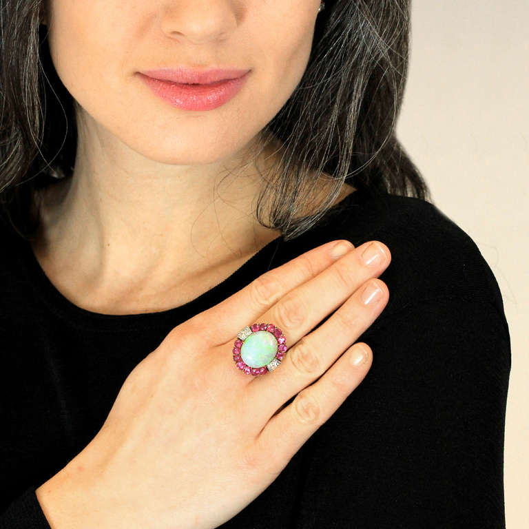 This stunning twenties confection is set with a scintillating 7.5 carat opal. Deliciously vivid greens, blues, and reds show fabulous movement of light, giving this stone gorgeous fire.  2.50 carats of vibrant pink red rubies and .25 carats of