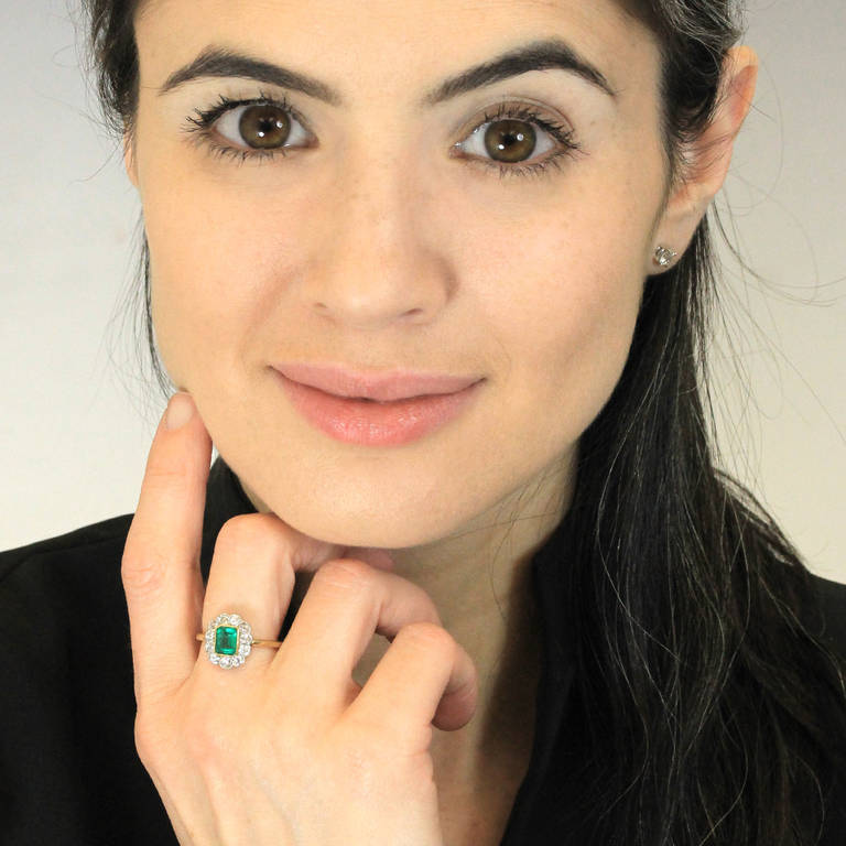 Circa 1910, 18k and platinum. This delightful antique ring features a vibrant 1.0 carat emerald surrounded by 1.08 carats of brilliant white diamonds. Treasured for its romantic and feminine look, this classic motif is as au courant today as it was