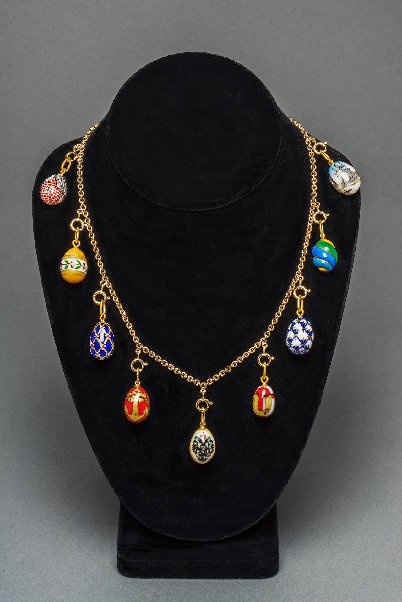 This beautiful Easter egg necklace is designed as a classic 14k yellow gold link chain suspending nine hand painted egg pendants from St. Petersburg, Russia. In colorful porcelain depicting a Romanov double-headed eagle-symbol of Imperial Russia, a