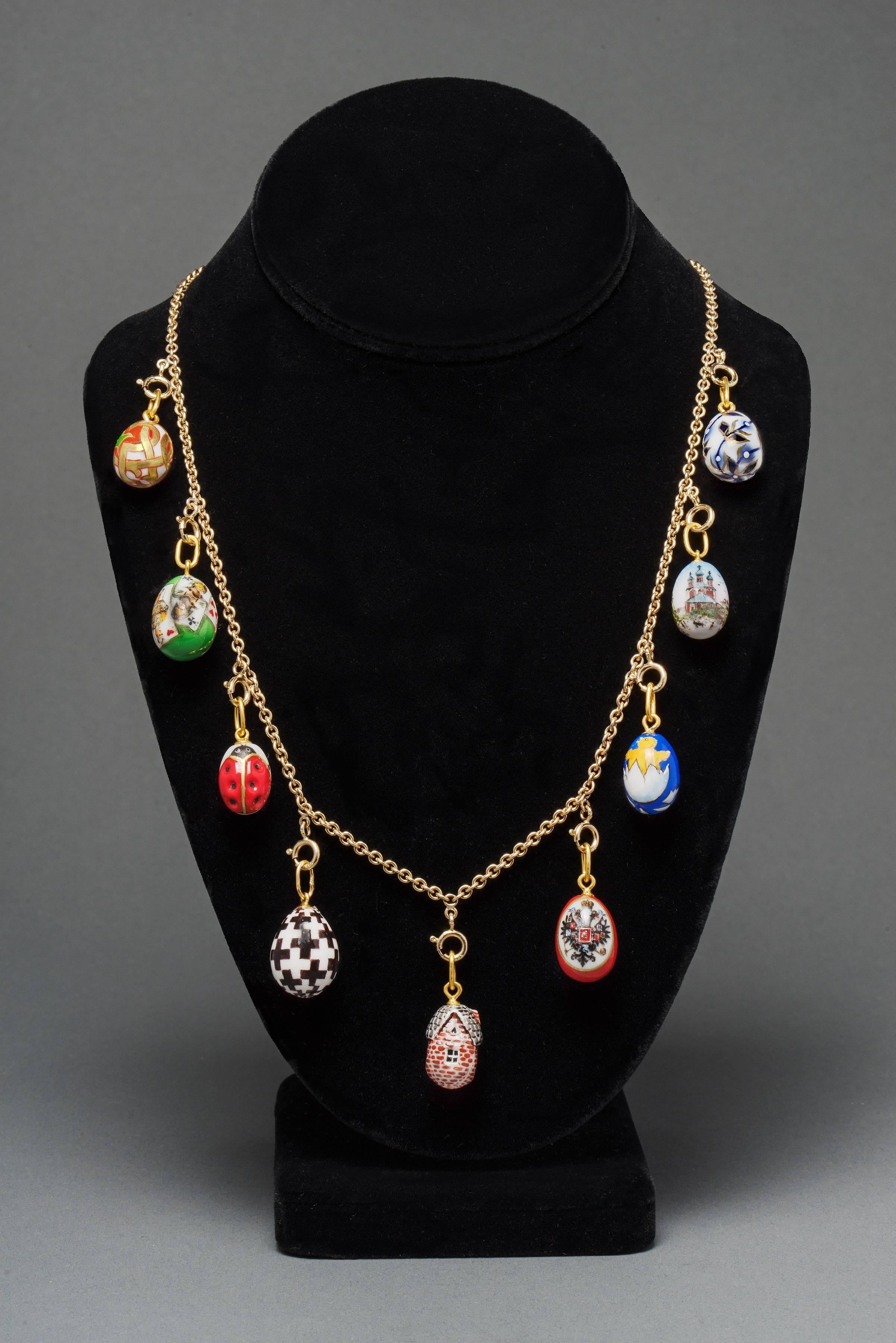 Designed as a classic gold link chain suspending nine hand painted egg pendants from St. Petersburg, Russia. In colorful porcelain depicting a fairy tale dacha with thatched roof, a Romanov double-headed eagle and a landscape of Russian churches