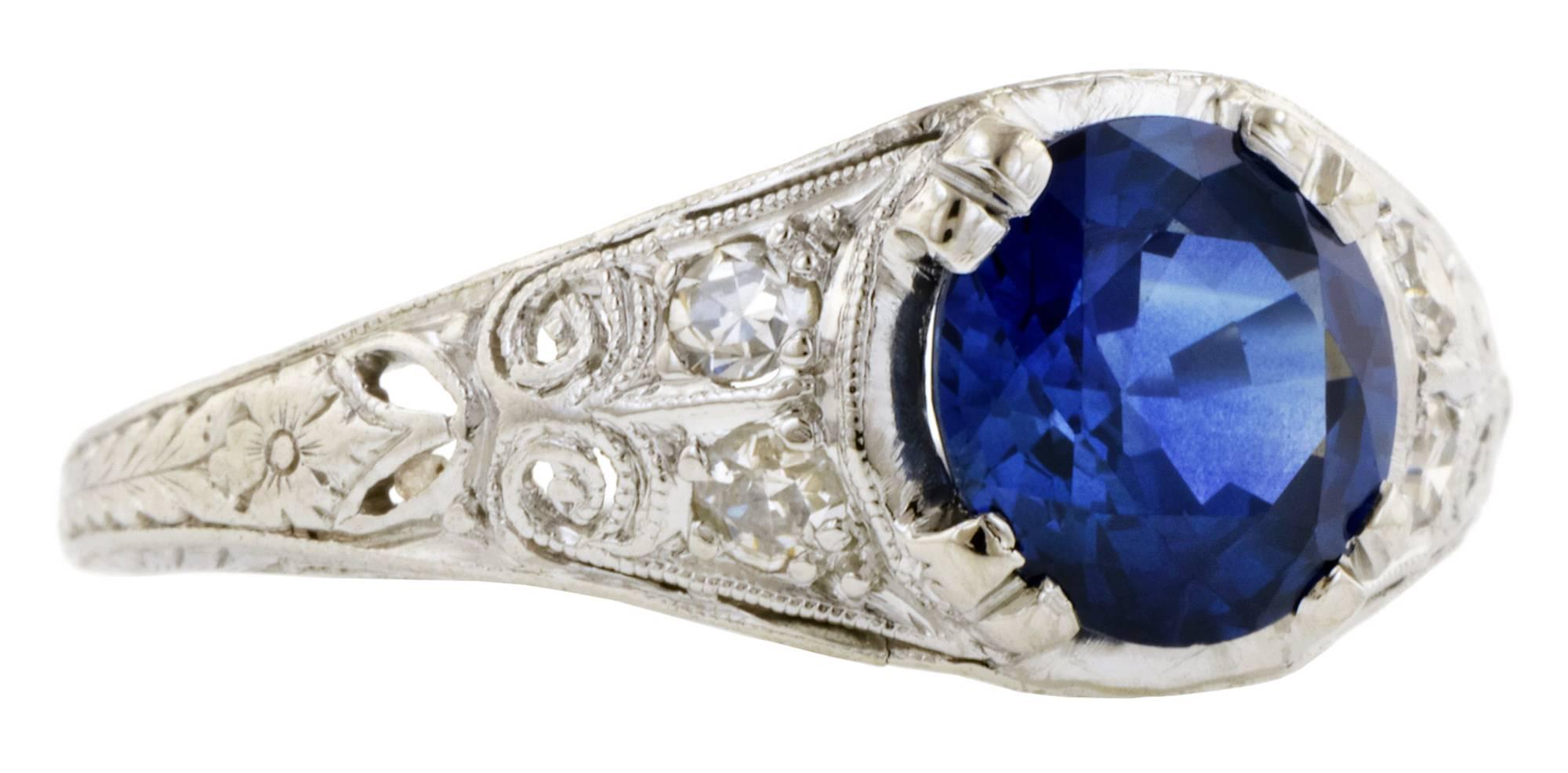 Art Deco sapphire ring centering a round sapphire weighing app. 1.66ct, flanked by four Single cut diamonds weighing app. 0.10ctw., in a tapered, filigree design with engraved flower & wheat detail on shoulders, fashioned in platinum. Circa 1935.