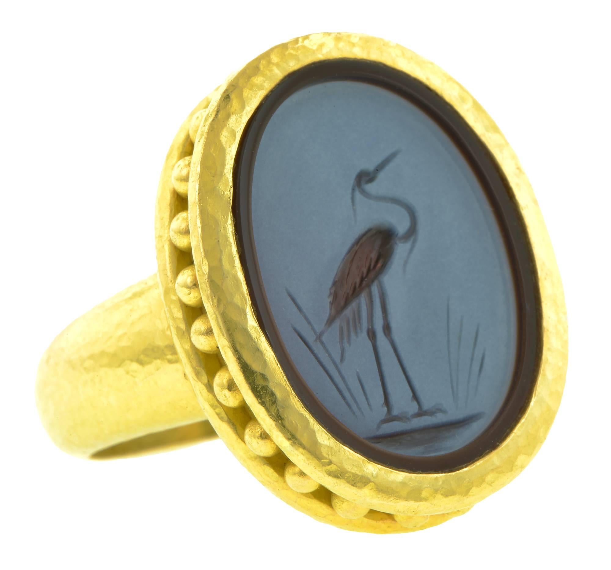 Estate Elizabeth Locke intaglio ring centering a collet set oval Venetian Glass intaglio measuring 20 x 15 x 4.8mm; featuring a carved Heron in wetlands theme. Etruscan motif, with granulation accents and hammered finish. Fashioned in 19k yellow