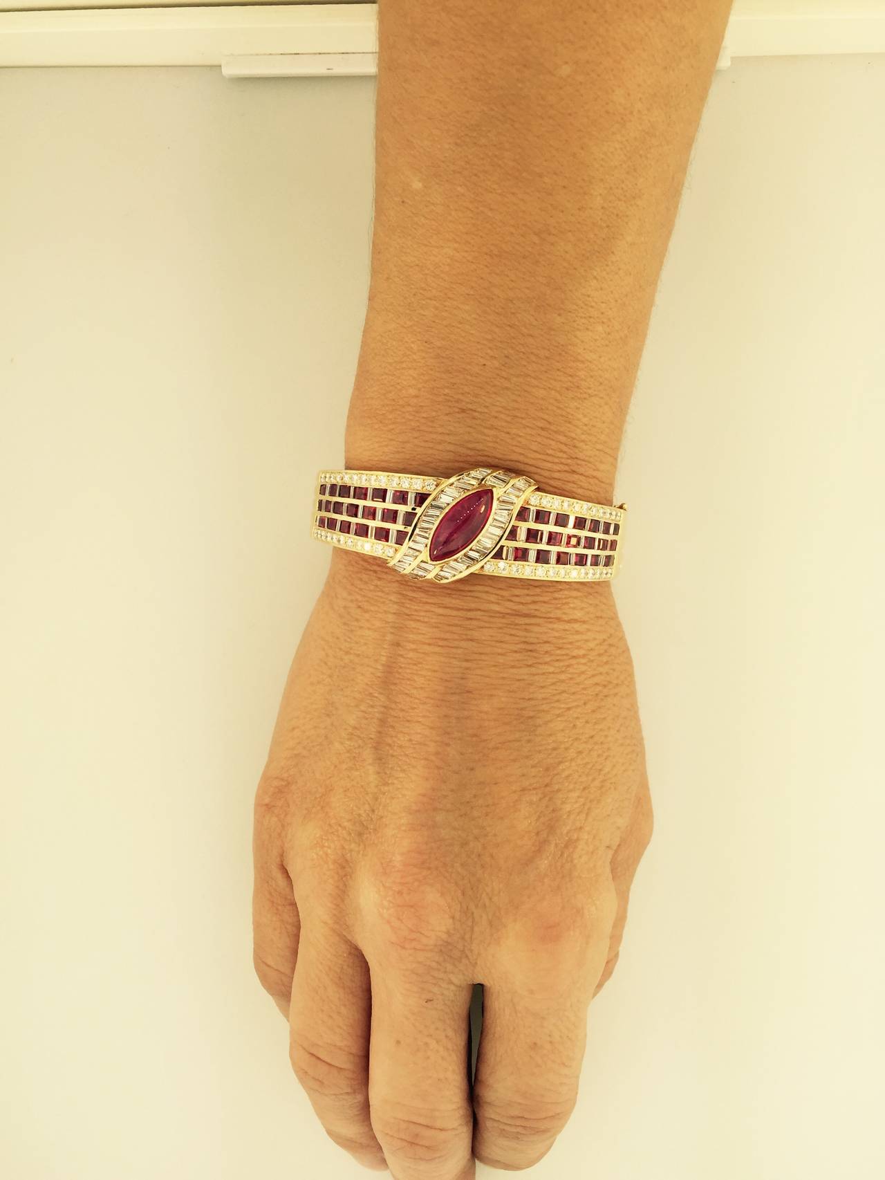 A Marquise Burmese cabochon ruby 3ct estimated set atop a wide 18k yellow gold bangle bracelet. GIA report #2161204998  No indication of heating.
Numerous diamonds and square cut Burma rubies, pave and channel set.
Estimated: 5ct total weight of