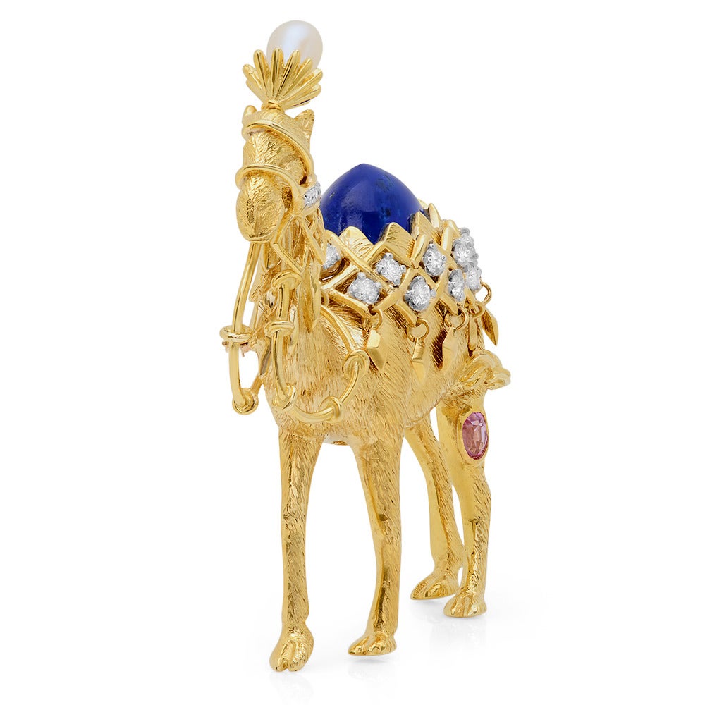 A diamond and multi gem brooch, by Jean Schlumberger, Tiffany & Co.
Designed as a textured 18k gold camel with a cultured pearl headdress, a lapis hump, accented by circular-cut diamond blanket and harness, the back leg enhanced by an oval pink