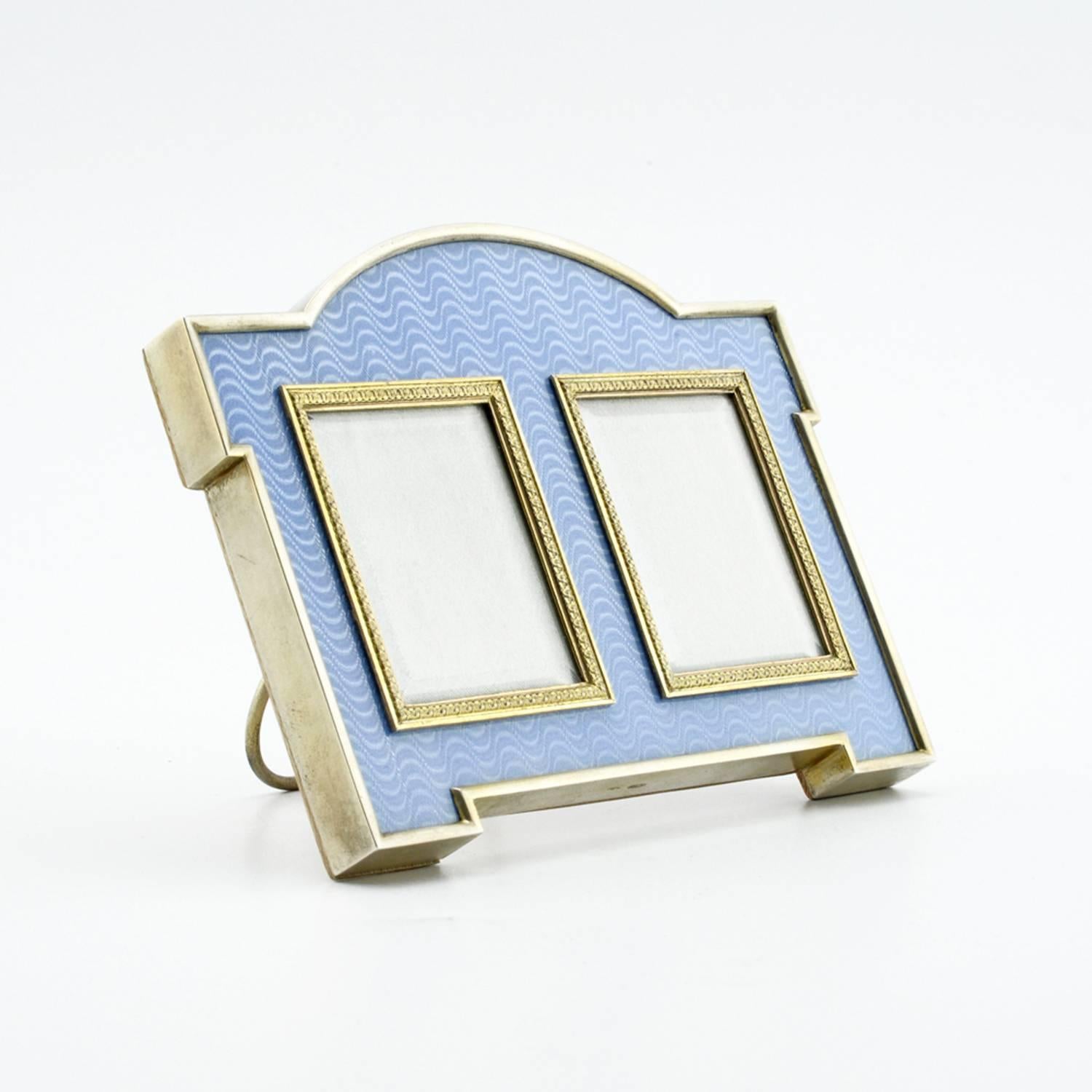 A Fabergé gilded silver and guilloché enamel double aperture photograph frame, workmaster Karl Gustaf Hjalmar Armfelt, St. Petersburg, circa 1904-1908. Shaped rectangular with bracket feet, the two rectangular apertures with leaf tip bezels,