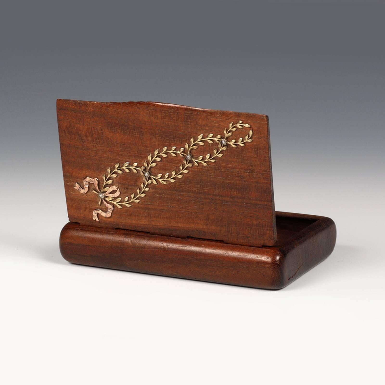 A Fabergé two-color gold-mounted palisander wood cigarette case, Moscow, 1899-1908. The rounded rectangular body carved from palisander wood, decorated in Neo-Classical taste with hinged lid diagonally applied with two interlocking yellow gold