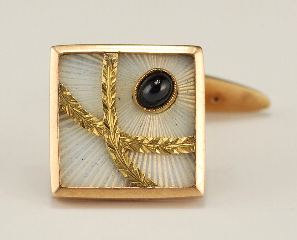 A pair of antique Russian two-color gold, transparent enamel, and sapphire cufflinks, Saint Petersburg, circa 1908-1917. The square links enameled translucent white over a sunburst engine-turned ground, the upper corners set with oval cabochon