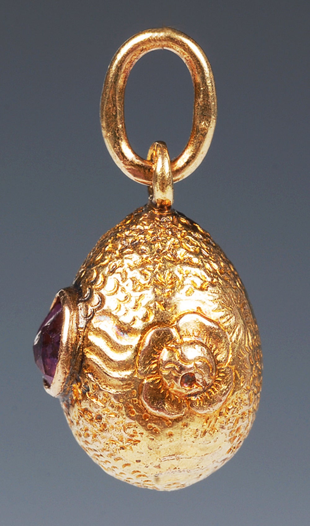 A Russian gold pendant egg set with an amethyst, maker's mark unclear, circa 1900. The repousse and textured body also decorated with raised gold flower heads. Height: 3/4