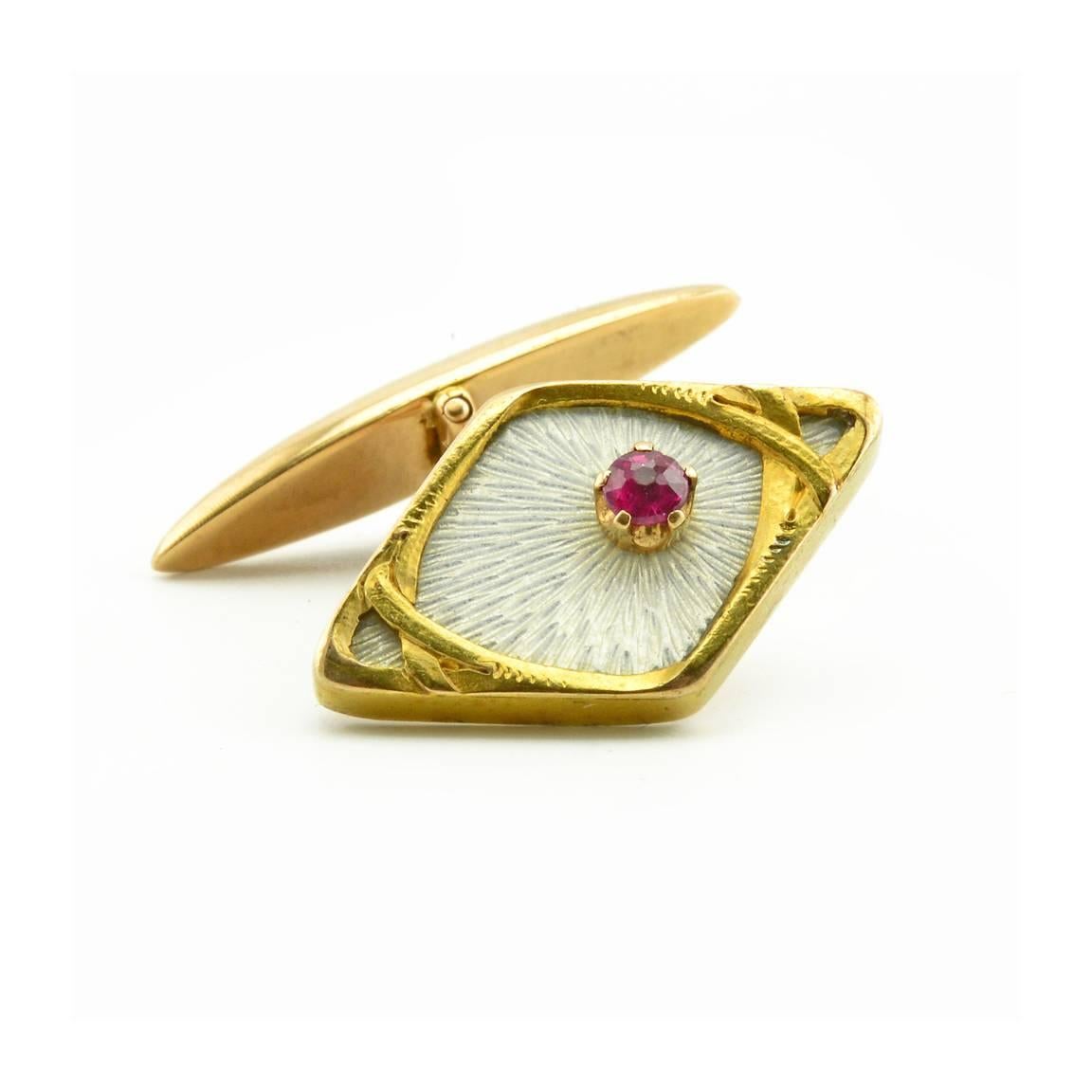 A pair of Russian gold, translucent enamel, and ruby cufflinks, St. Petersburg, 1908-1917. In Art Nouveau taste, the links of navette form, enamelled translucent white over a hatched sunburst ground and with rose cut rubies set off center, all