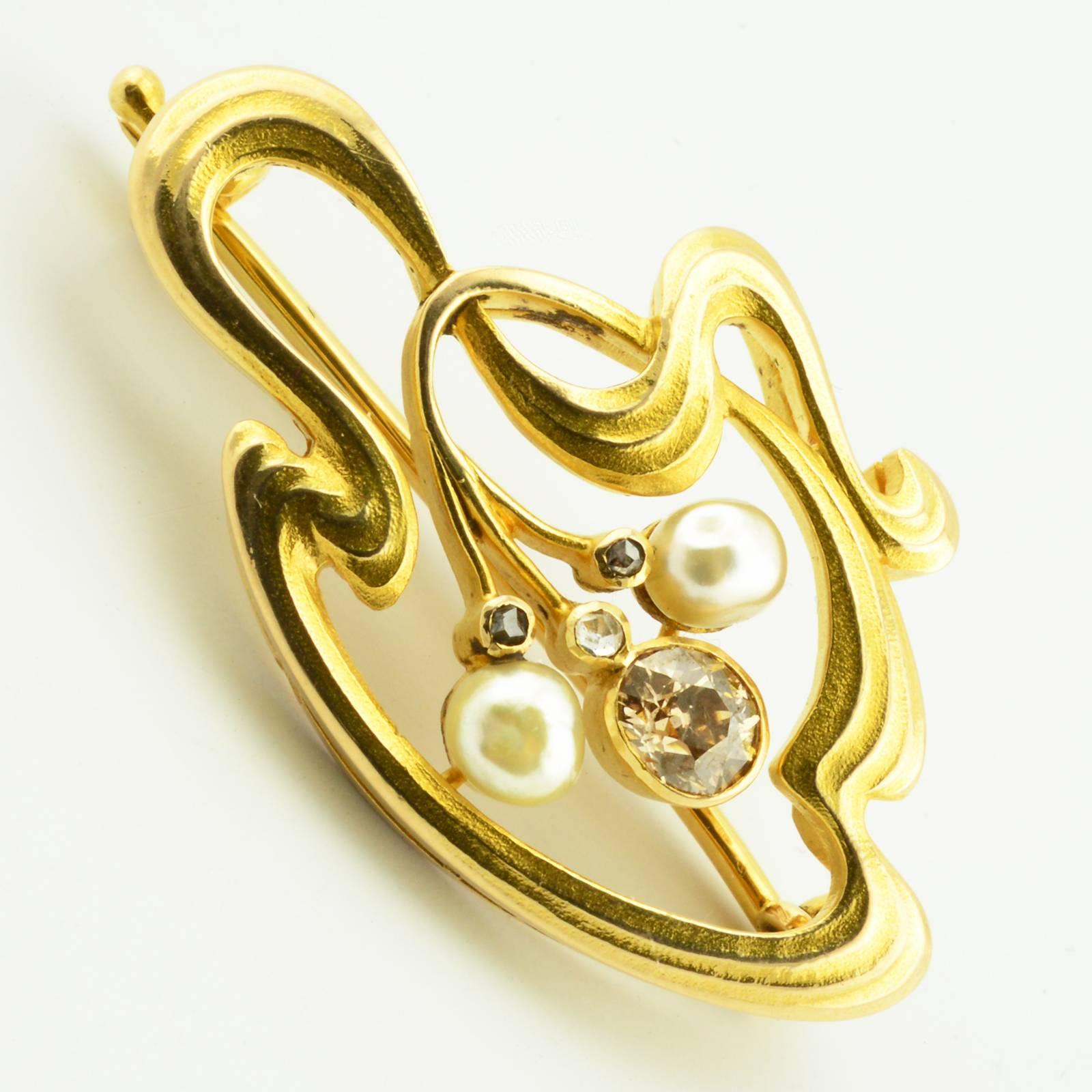 An antique Russian Art Nouveau gold, white diamond, brown diamond, and pearl brooch or pin by Imperial Court Jeweler Karl Bok (Bock), St. Petersburg, 1899-1904. The brooch cast and chased in Art Nouveau taste as a continuous oval whiplash