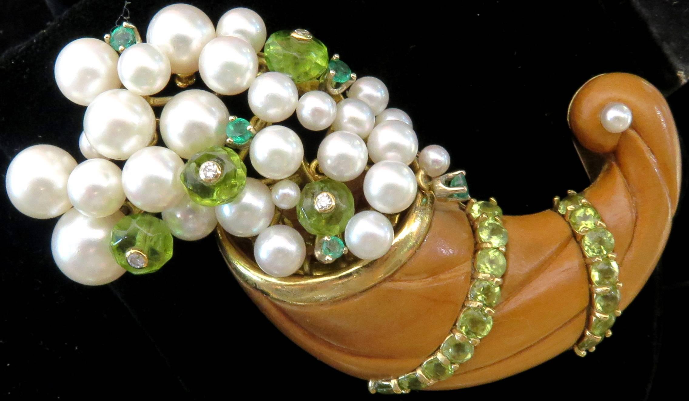 This classic design 18k Seaman Schepps Cornucopia is quite unique in that the pearls emeralds and faceted peridots with inset diamonds all have movement. They appear to be coming out of the wooden vessel. 
This pin measures approx 3 inches by 1 1/2