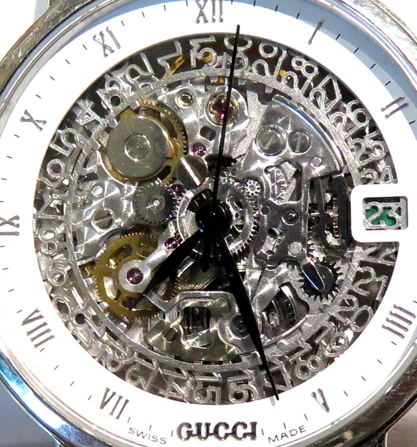 This Platinum Gucci wristwatch is just so out of the box!  The skeleton dial with white enamel border, roman numeral indicators, and date aperture, enclosing an automatic 21-jewel movement, display back, 32 mm, with a signed Gucci black leather