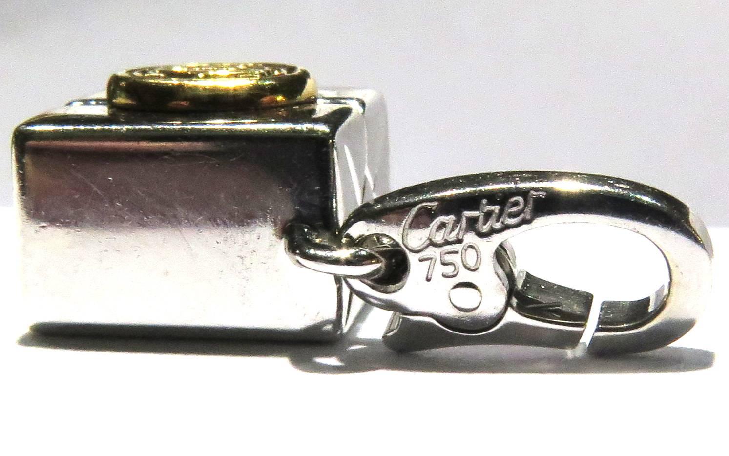 This classic Cartier pendant or charm has it's attached bale that can be put on a bracelet or necklace. It is all 18k white gold with an attached double C logo in yellow gold on top. It has a gift wrapped motif. On the bale is also signed Cartier