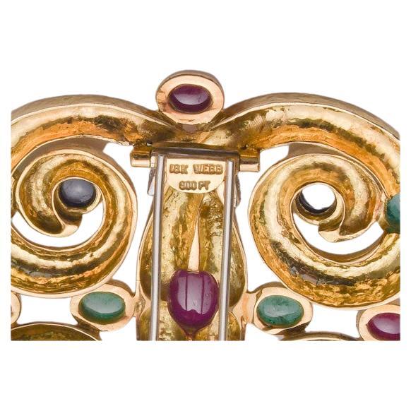 This brooch is a 1970's traditional WEBB design. Interlocking curled ram horn design accented by twelve round brilliant diamonds totaling approx. 0.76ct. one central, oval cabochon ruby, approx. L.9.77 x W.6.60mm; six emeralds, four blue sapphires,