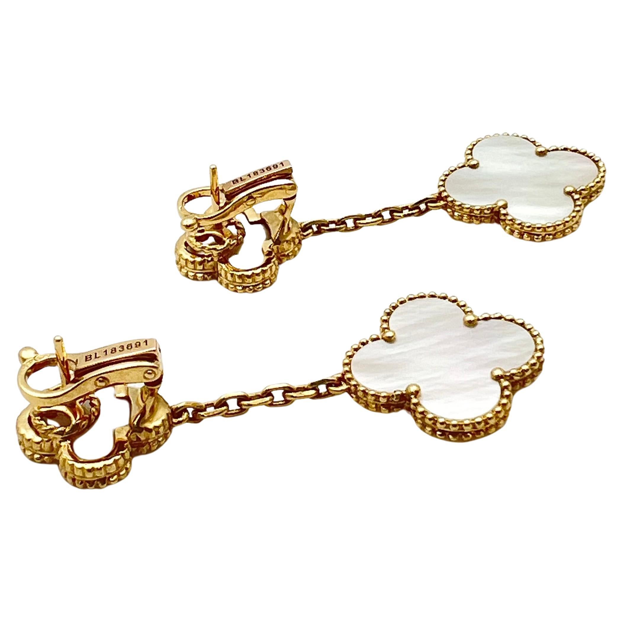 Van Cleef & Arpels Magic Alhambra drop earrings in 18k yellow gold, featuring a smaller mother-of-pearl clover-shaped motif at top and larger mother-of-pearl clover-shaped motif at bottom.  Clip backs with removable posts for pierced or unpierced
