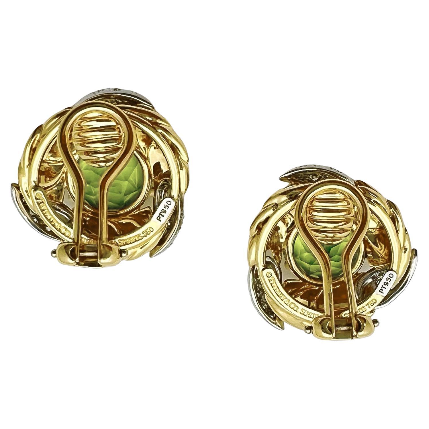 Designed by Jean Schlumberger for Tiffany & Co, these clip earrings each center a round peridot set within a wreath of 18k yellow gold and platinum.  The earrings are further accented by colorless round brilliant-cut diamonds.  Peridot measuring
