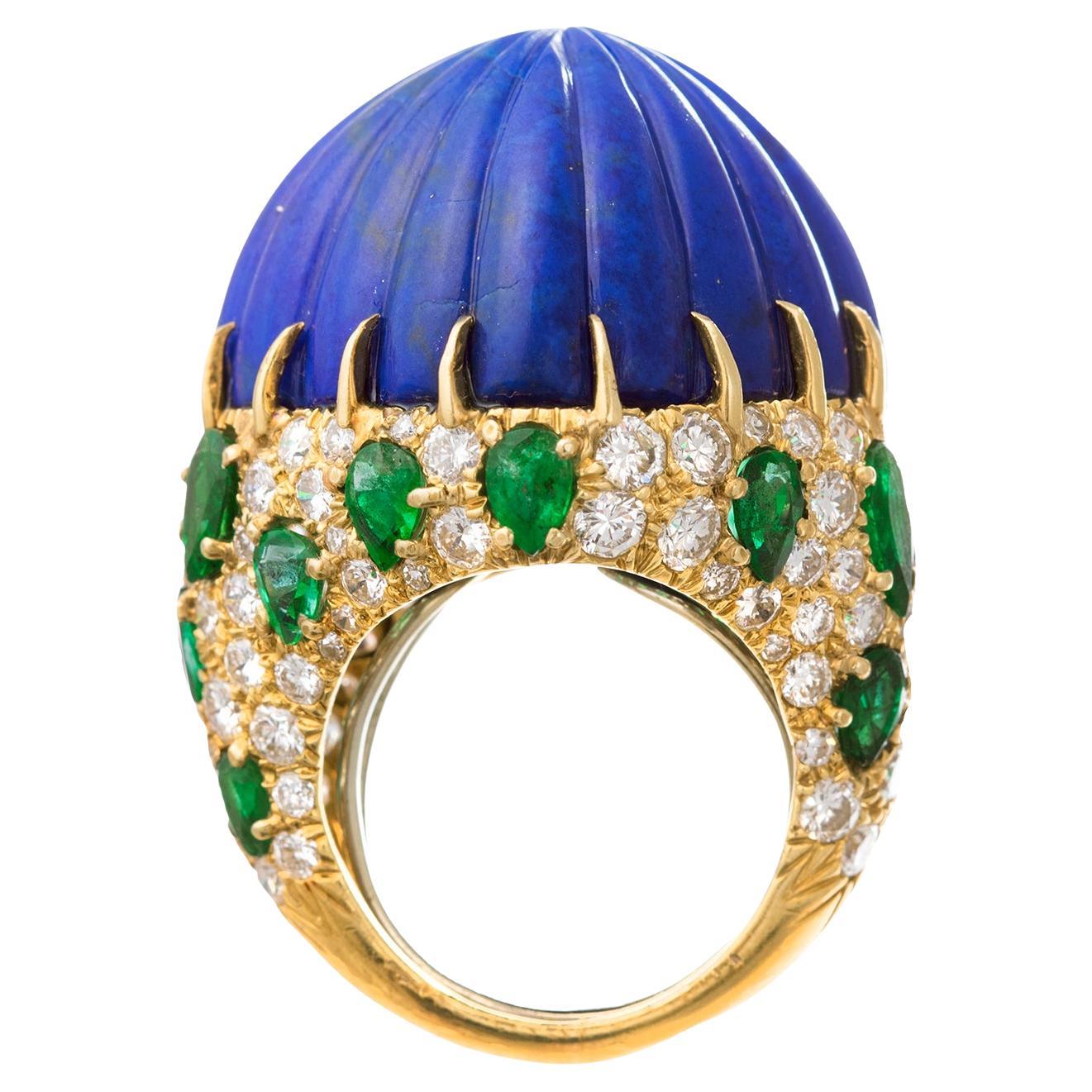David-Webb-Cocktailring aus 18 Karat Gelbgold mit einem geschnitzten kissenförmigen Lapis im Cabochon-Schliff in der Mitte, umgeben von birnenförmigen Smaragden in Pflasterfassung und runden Diamanten im Brillantschliff.  Der Lapis misst 22 mm im