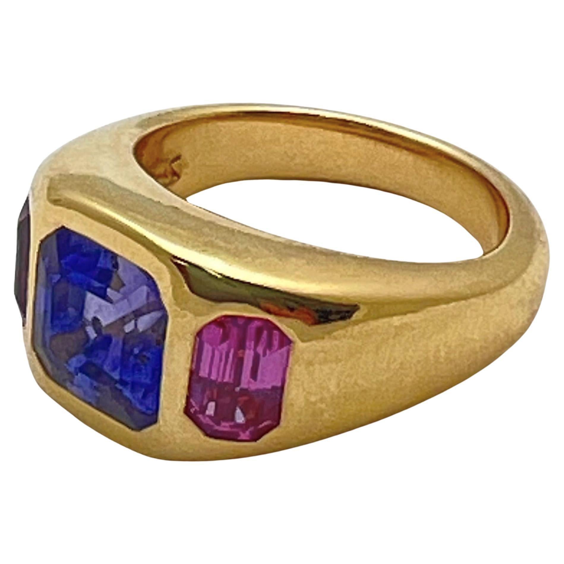Anello in oro giallo 18 carati in stile gitano con zaffiri rosa e viola.  Montatura in oro giallo 18 carati lucidato a specchio  con uno zaffiro naturale blu violetto, taglio a gradini, stile asscher, del peso di 3,56 carati.  Accompagnato da due