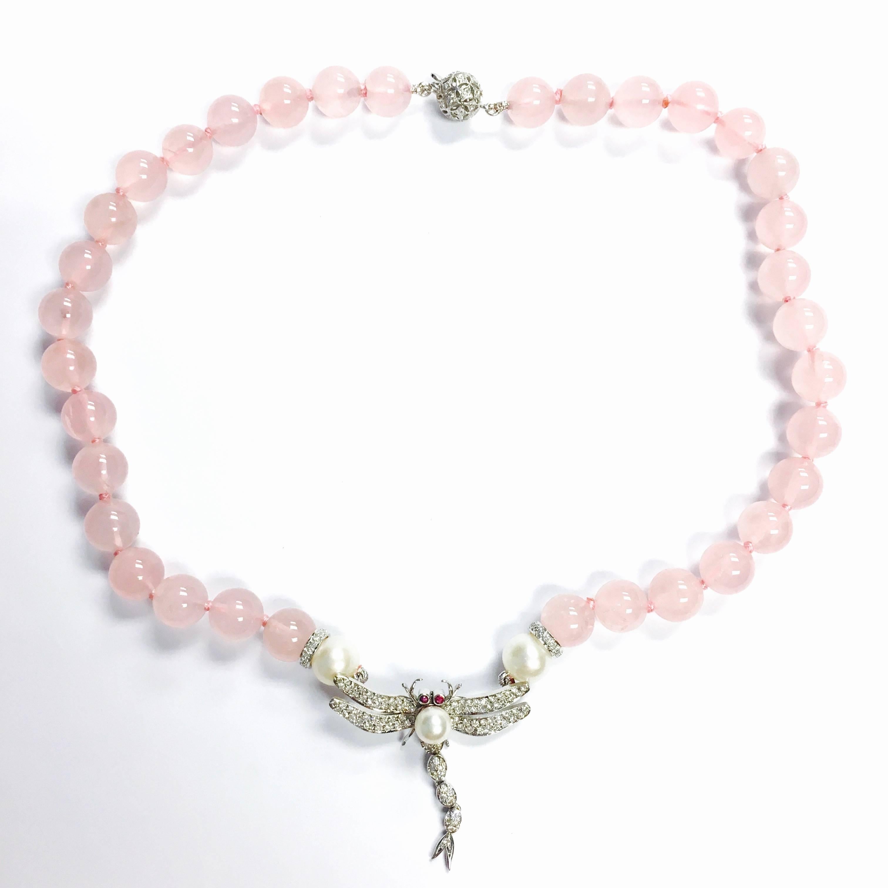 The Necklace features a 14K white gold diamond set articulating dragonfly with  pearl body and ruby eyes, supported by two 10 mm white cultured pearls, diamond set spacers and a strand of 10 mm round rose quartz bead strand. Seventeen inch length