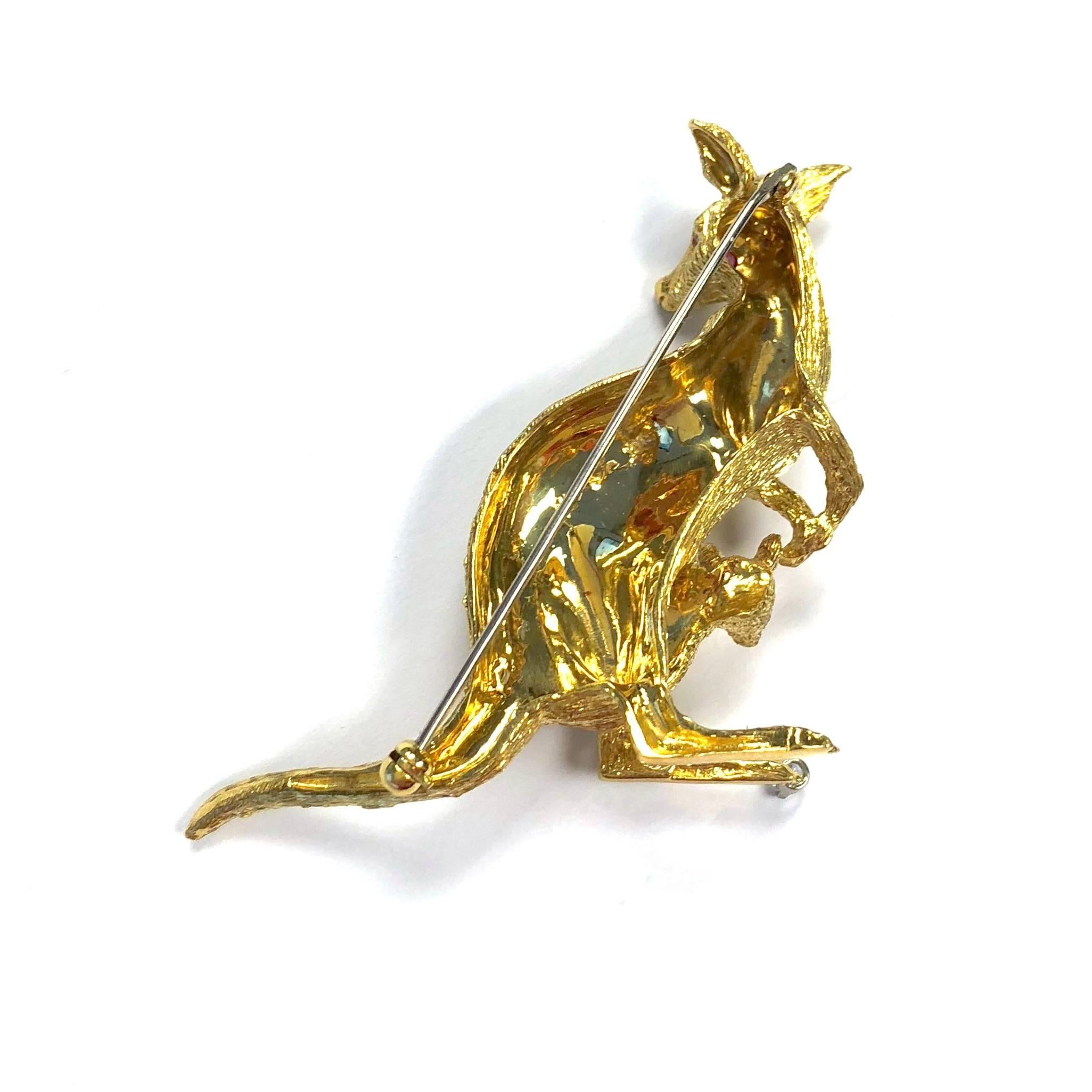 A beautifully textured 18k yellow gold pin featuring a kangaroo with her joey, a mother and child in a loving embrace. Accented with ruby eyes and a  0.06 ct round brilliant cut diamond solitaire. 
Marked: 18K PP (trademark)
Measurements: 1 5/8