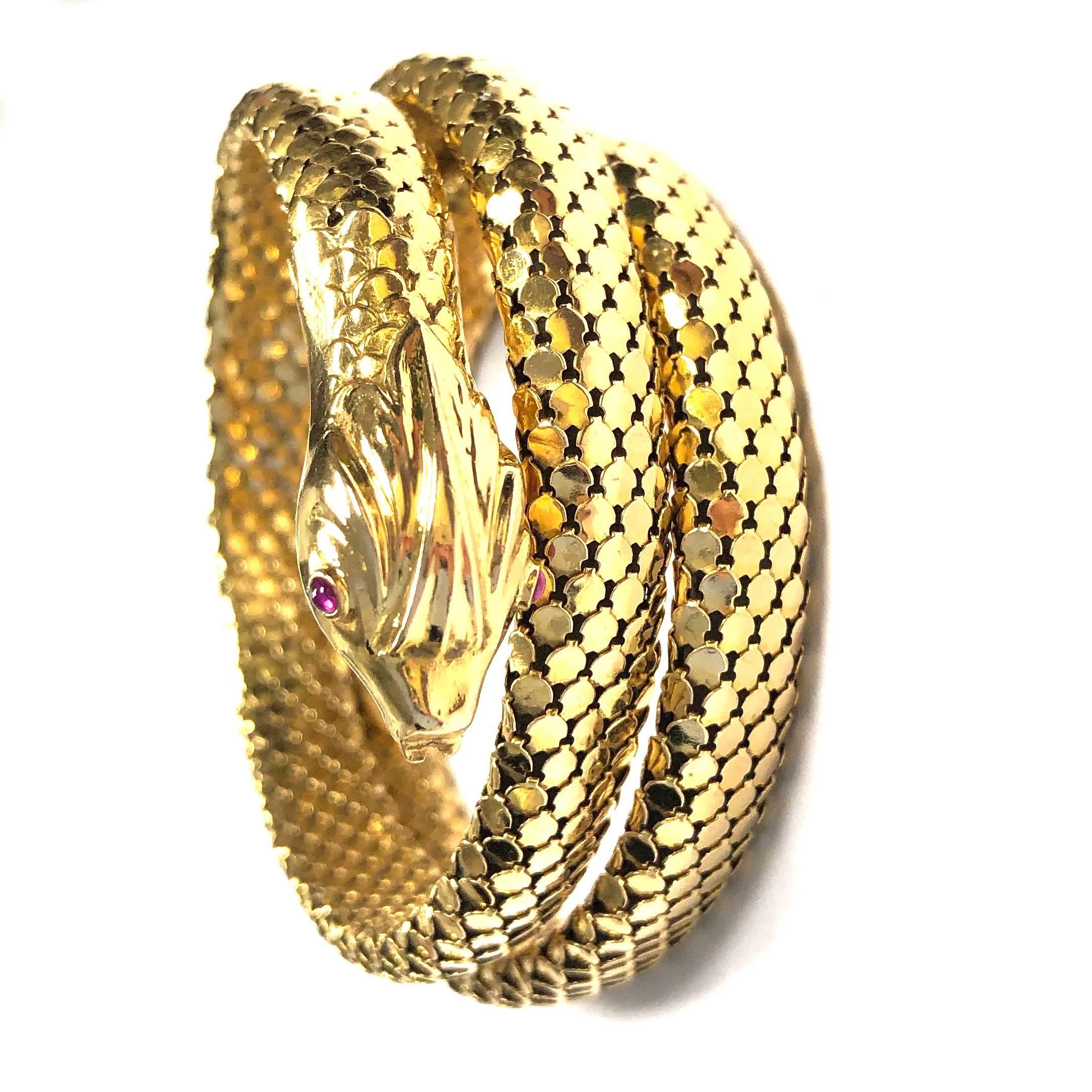 Crafted in 18kt yellow gold, comprised of the body of a serpent which coils three times around the wrist. The body is textured with small gold plaques piece together to represent scales. The head of the snake has a three-dimensional design with ruby