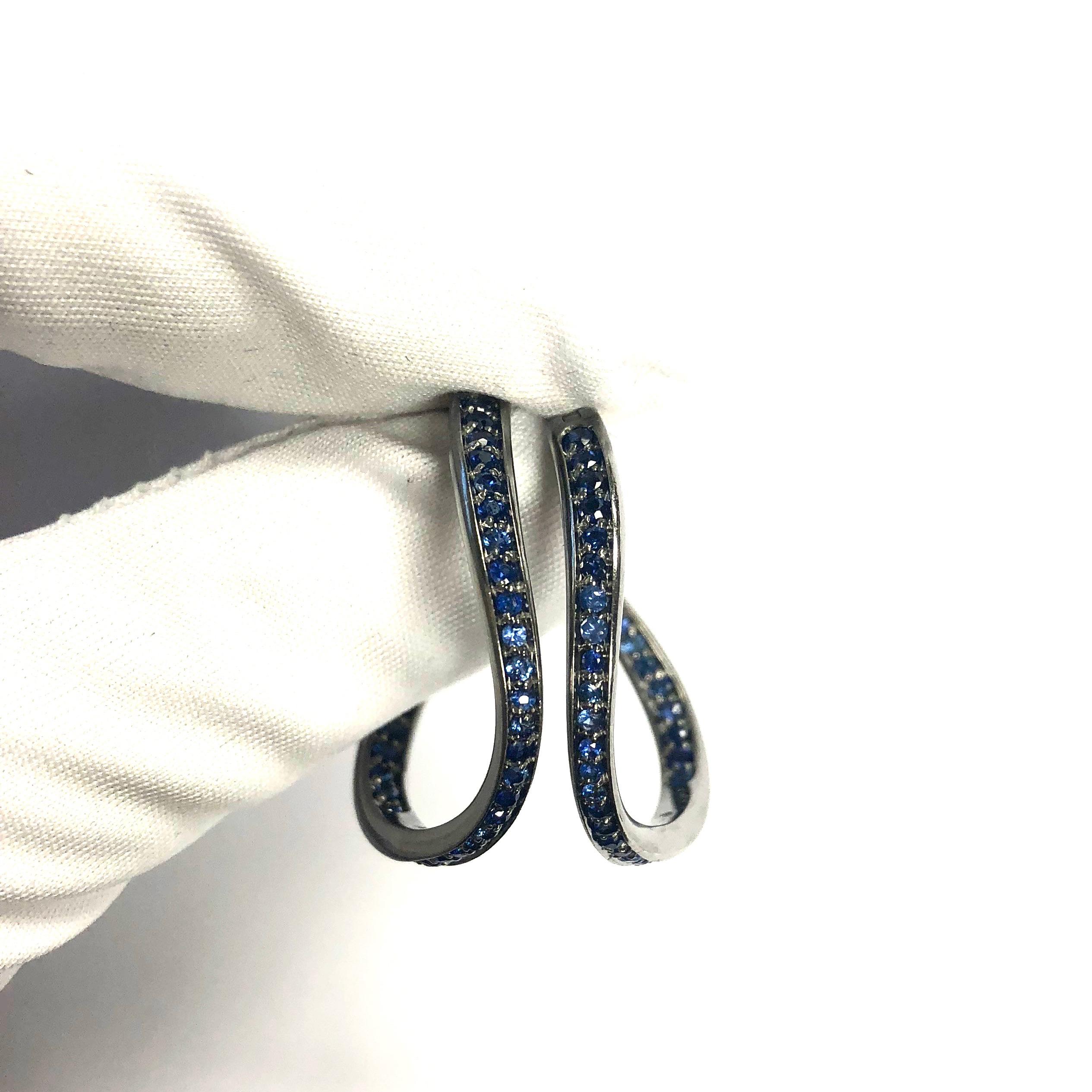 Crafted in 18K white gold with black rhodium finish, each earring features a curving hoop design set with forty round cut rich blue sapphires.
Approximate total sapphire weight: 2.5 carats.
Measurements: 
Diameter: 1 3/16