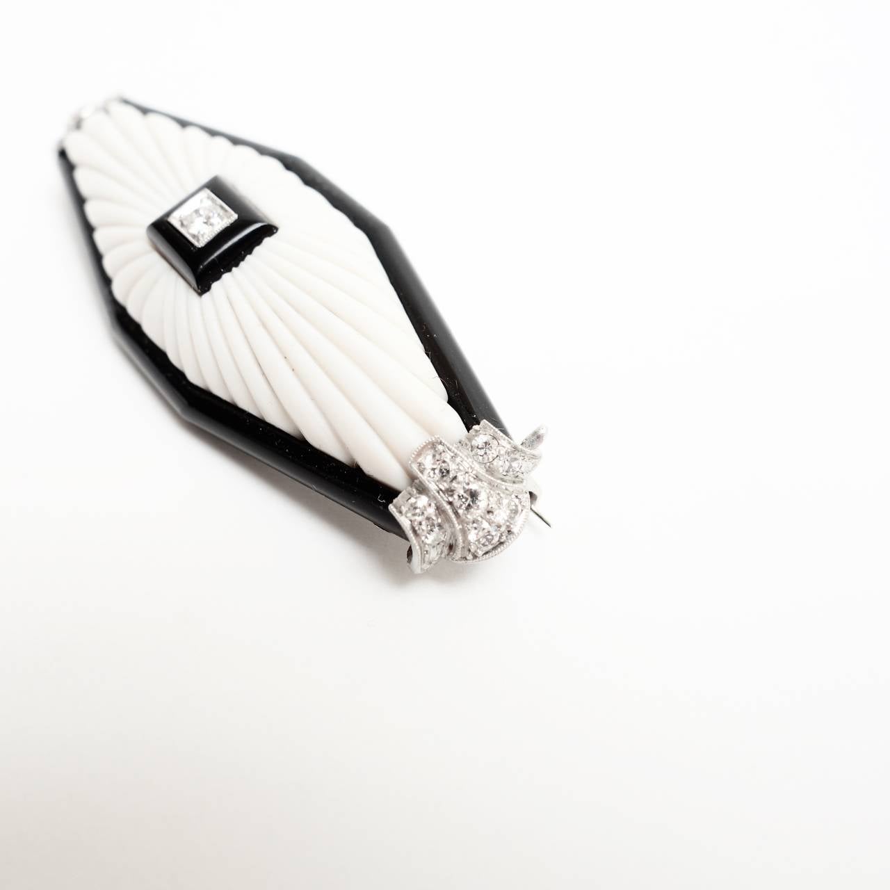 Amazing white coral, black onyx and diamond brooch with 18K white gold and platinum.  Featuring an elongated hand carved white coral set with a diamond and black onyx center piece, framed by black onyx and two diamond set end pieces. All diamoonds