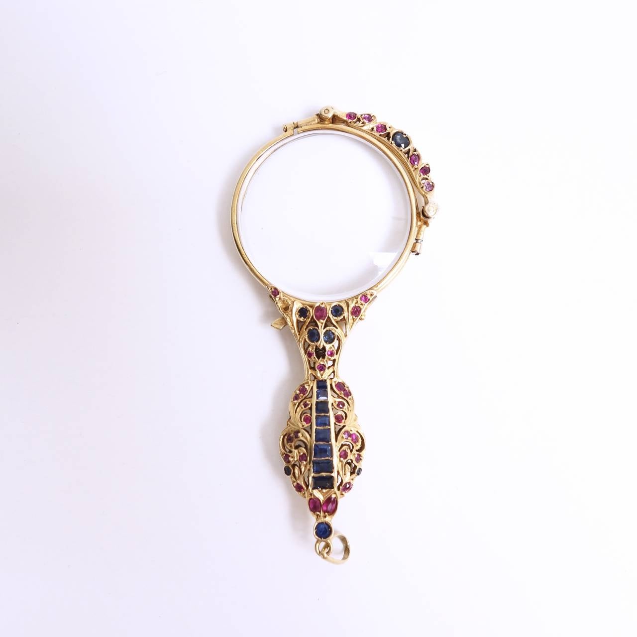 This unique antique lorgnette displays an open-work design handle set with natural blue sapphires and rubies. Crafted in 14K yellow gold with a spring activated opening and closing mechanism. 
There are 16 sapphires an 34 rubies, approximate total