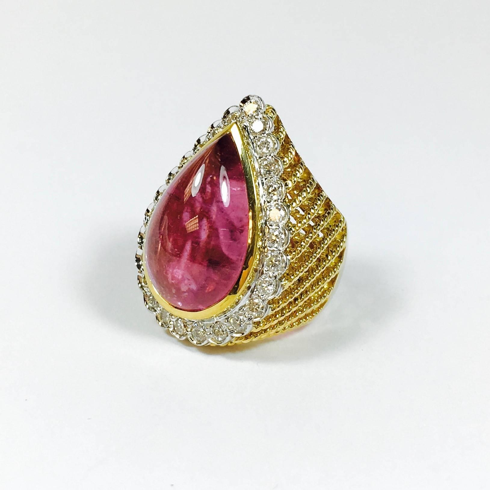 This beauty features a teardrop shaped 22 x 14 mm, approximately 20ct pink tourmaline cabochon set within a bezel of diamonds, supported by lattice design gold gallery, completed by a 6 mm wide gold band. 14K gold. Excellent workmanship. 
26 round