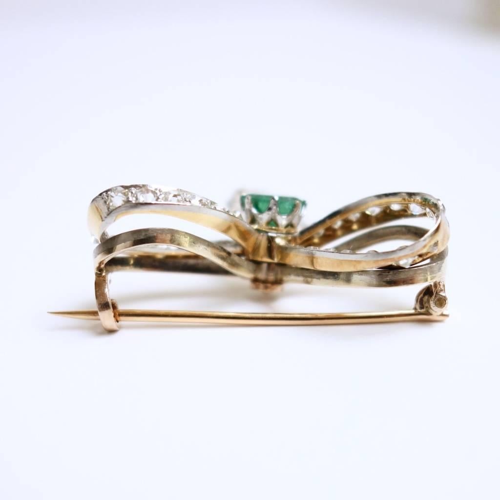 Fairy Victorian brooch crafted in Platinum and 14K yellow gold, featuring an approx.  1.25ct emerald solitaire supported by three diamond set ribbons. There are 43 old mine cut diamonds, approximate total weight of 3.00 ct. 
The brooch can easily