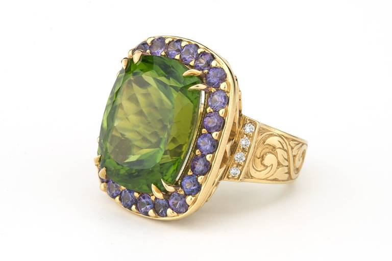 One-of-a-kind, hand-carved ring featuring 24.0 carat Pakistani Peridot center-stone, 2.58 carats of unheated purple Sapphire, 0.35 carats of Diamond, and 20.39 grams of 18K Yellow Gold. Hand-carved engraving on the sides of the shank.  An amazing