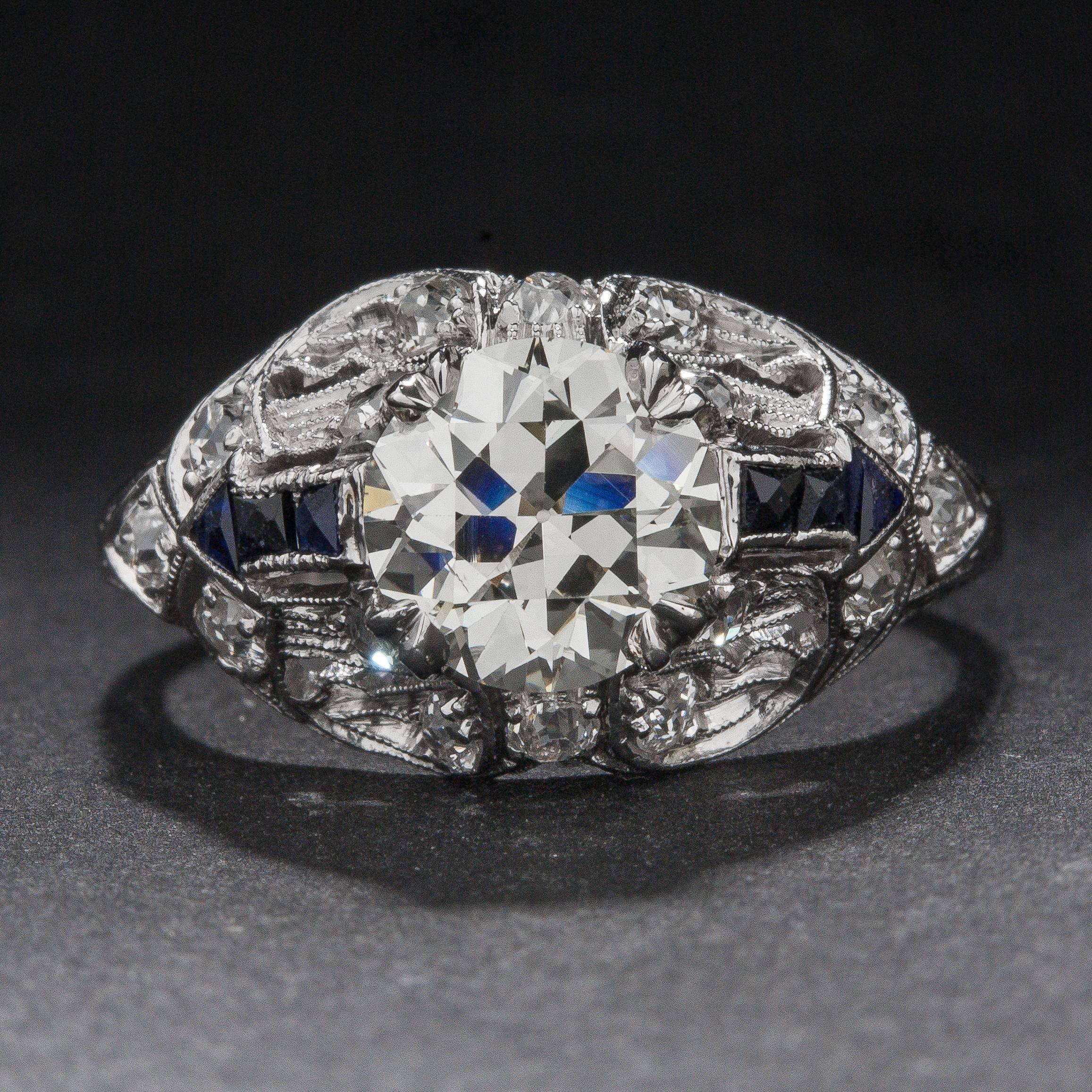 This stunning Art Deco era ring features a 1.38 carat Old European Cut center diamond (Estimated J color, SI1 clarity), 6 French Cut sapphires weighing a total of .12 carats, and 14 Old European Cut side diamonds for .16 total carats. The intricate