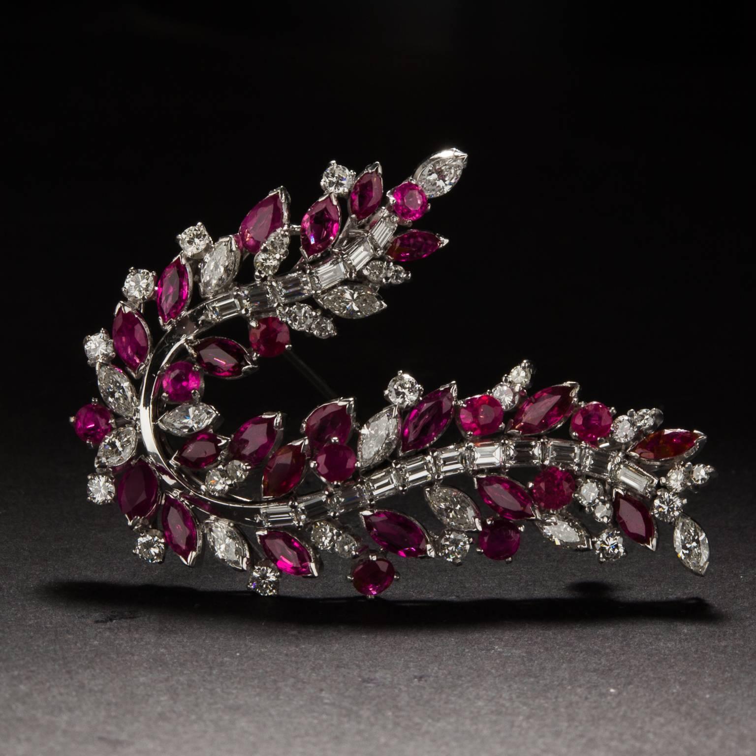 This brooch displays a graceful garland of plentiful rubies and diamonds. Crafted in 18 karat white gold, it houses 3 carats of rubies, in marquee and round cuts, and 2.5 carats of diamonds, in marquee, round, and baguette cuts. The variety of