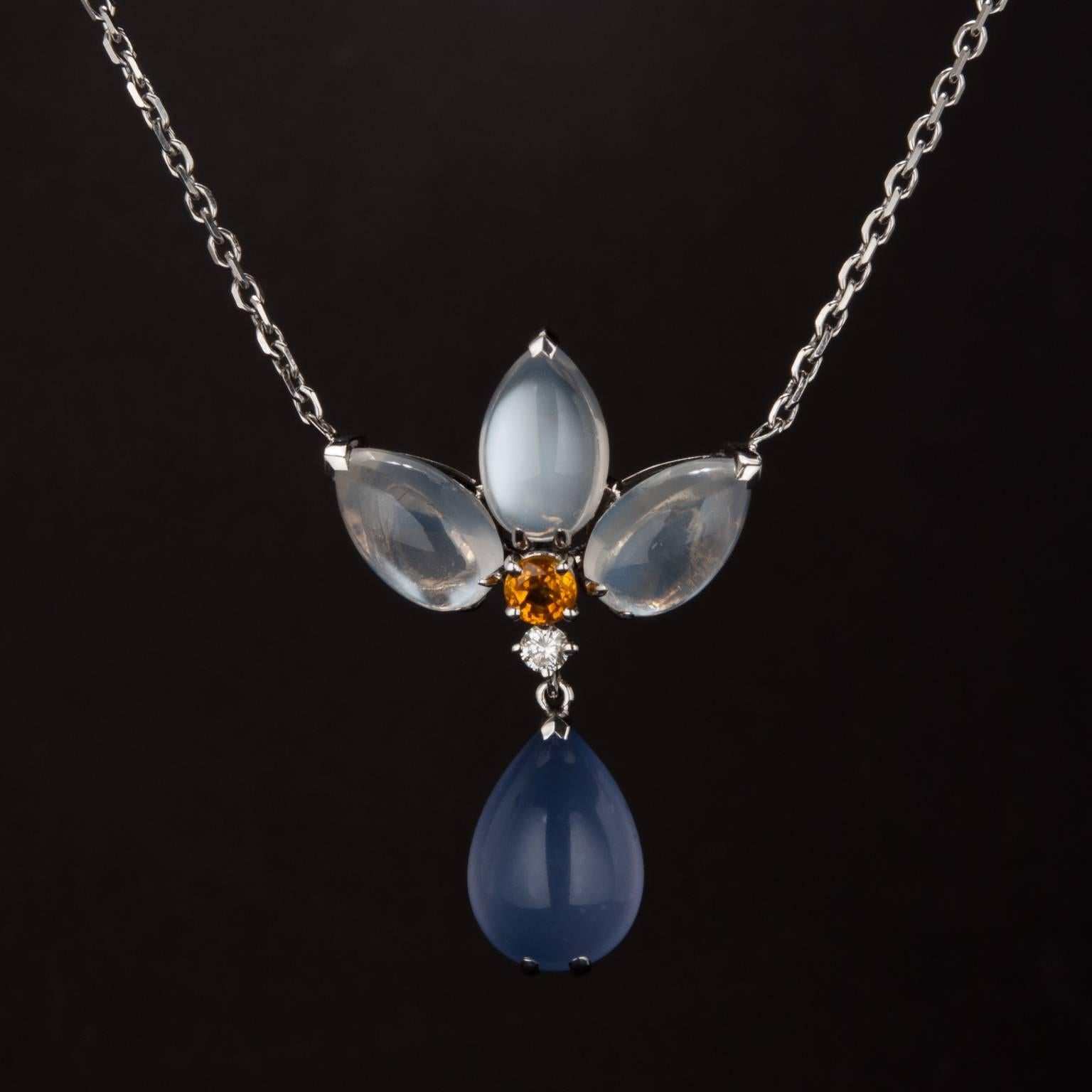 This gorgeous pendant features 9.00 total carats of white and blue moonstone, an eye-catching .10 carat orange sapphire, and a .06 carat diamond accent. The mounting is made in 18k white gold and the pendant rests on a fixed 16 inch 18k white gold
