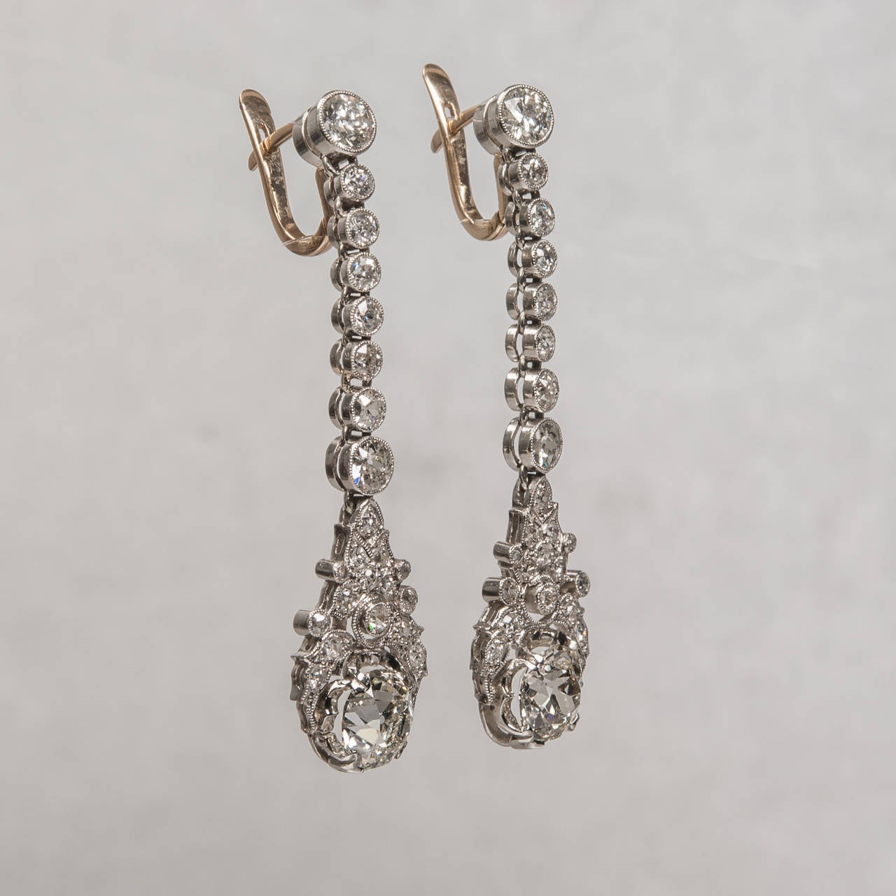 This stunning pair of Edwardian diamond dangle earrings is handcrafted in platinum with all original diamonds. The design features graduated bezel set round diamonds flowing down from the clasp into a lovely floral pattern which displays large Old
