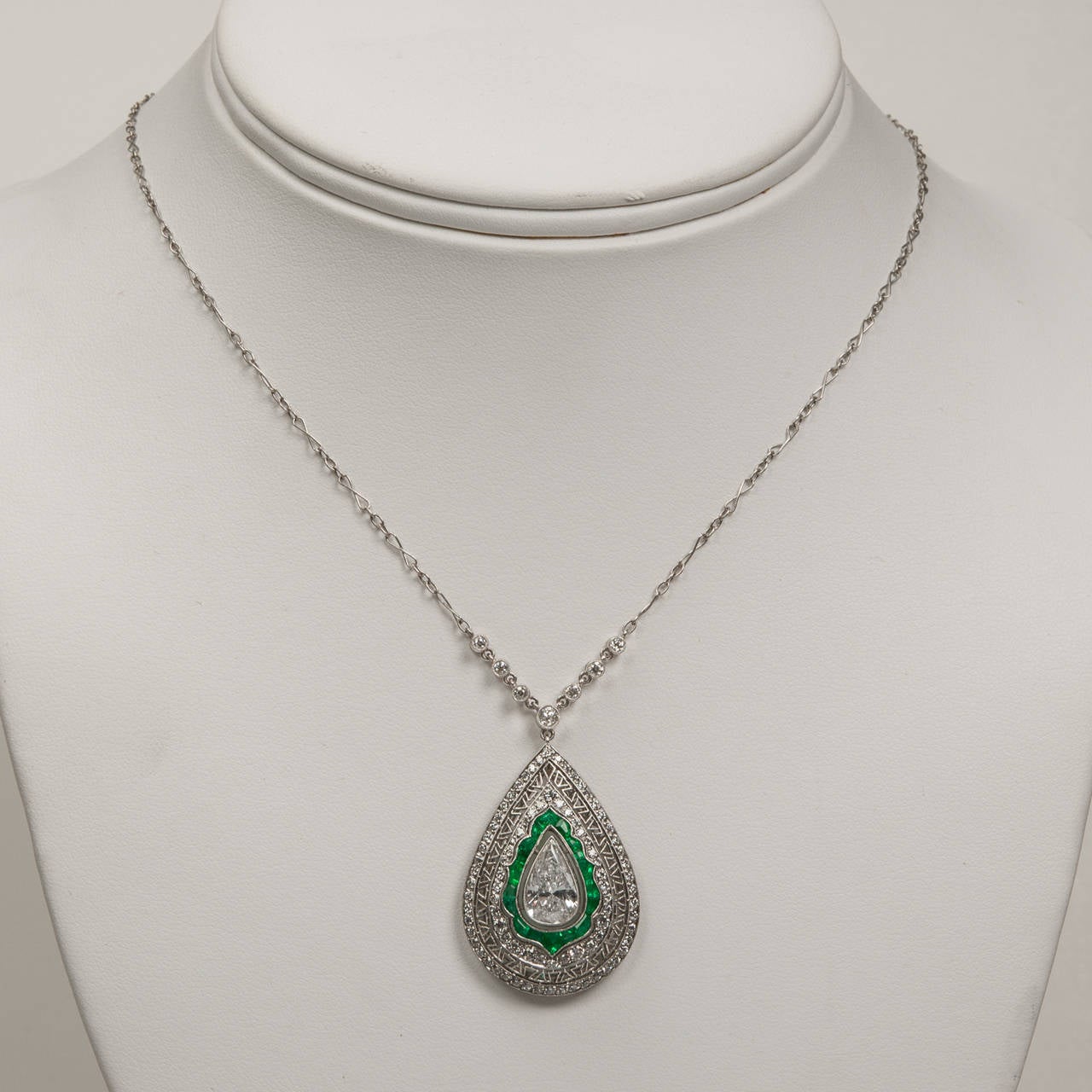 This newly made emerald and diamond necklace is handcrafted in platinum with bright white diamonds and colorful emerald gemstones in an Art Deco design style.  The pear shape drop has a stunning 1.55 carat center diamond (K color, SI2 clarity)