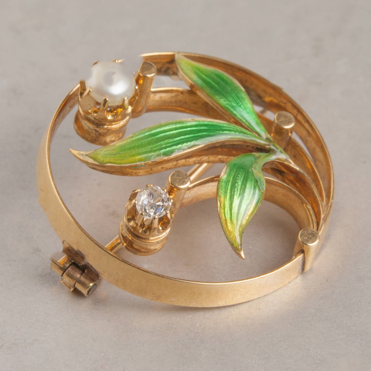 This lovely Art Nouveau pin features beautiful enamel work as well as diamond and pearl accents. The elegant floral design and exquisite enamel detailing exemplify the craftsmanship of the Art Nouveau design era. This piece is handcrafted in 14k