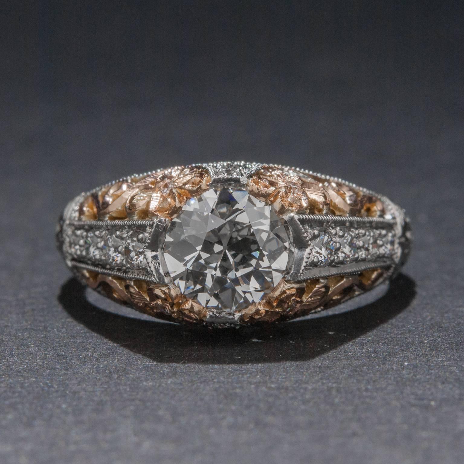 This stunning vintage style ring features a brilliant 1.01 carat center diamond (G color, VS1 clarity) as well as 12 side diamonds for .12 total carats. The platinum and rose gold mounting has intricate filigree work and milgrain detailing. This