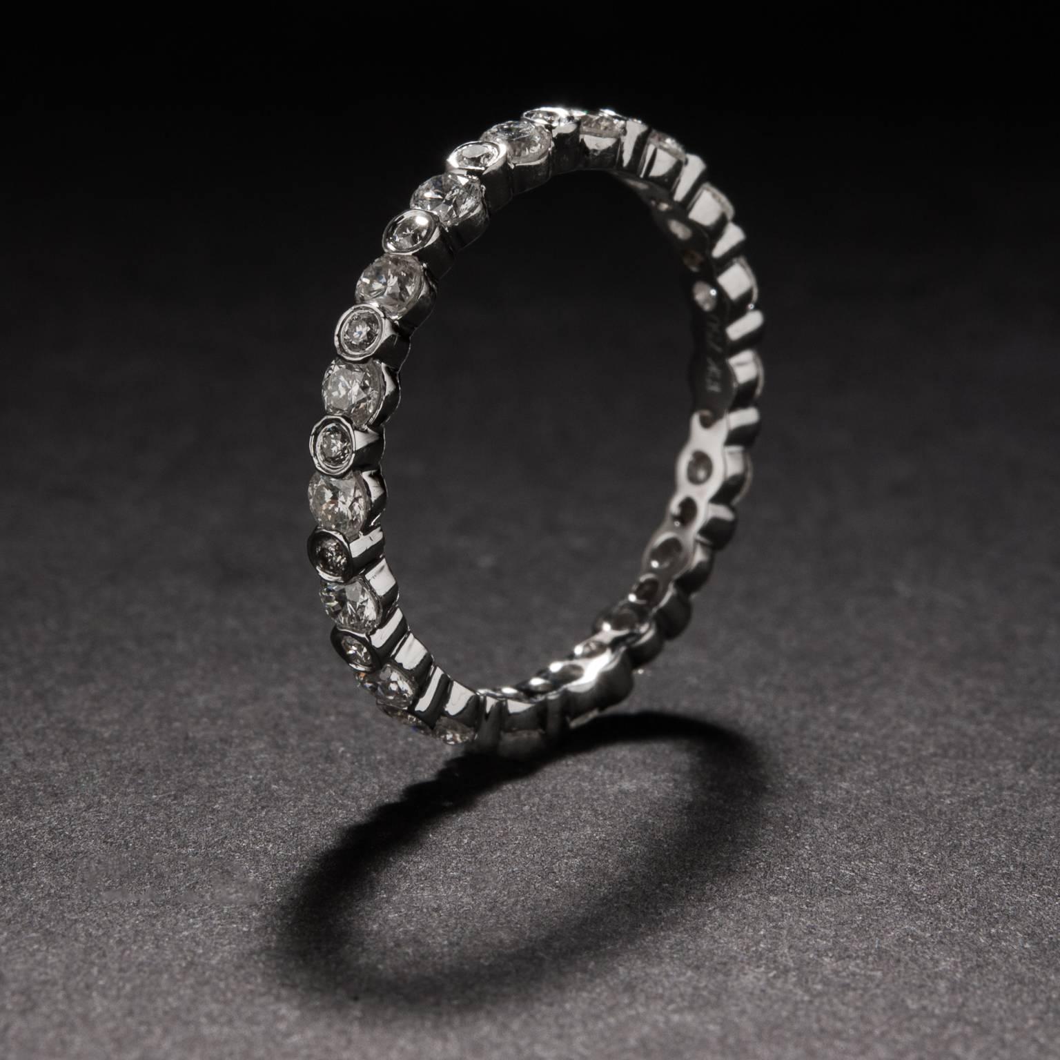 An elegant and eye-catching eternity band with 1.10 total carats of diamond. This ring is crafted in 14k white gold and features alternating larger and smaller stones, with the bezel setting of the smaller stones creating a channel setting for the