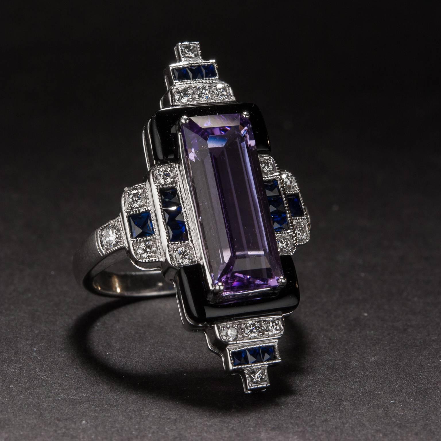An exceptional Art Deco style ring with a lovely 3.11 carat center amethyst. The center stone is accented by onyx as well as .79 total carats of sapphire and .25 total carats of diamond. The striking and angular mounting is crafted in platinum and