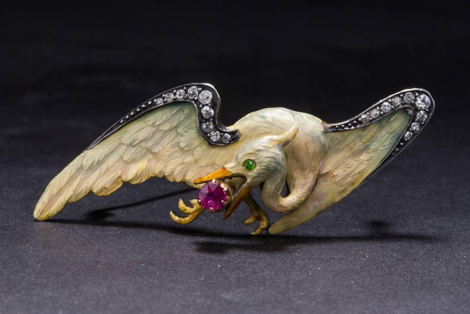 This exquisitely detailed Art Nouveau era brooch features an intricate hand-carved rose gold bird with enamel overlay. The piece features a single accent ruby, a single accent demantoid garnet, and .19 total carats of accent diamonds. The brooch