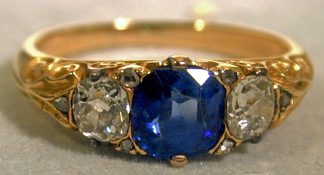 Sparkling Victorian cushion cut sapphire ring flanked by two cushion cut diamonds in a classic 18K yellow gold setting. The sapphire weighs approximately 1.20 carats and has a fine blue color. The diamonds have a total weight of .90 carats. There