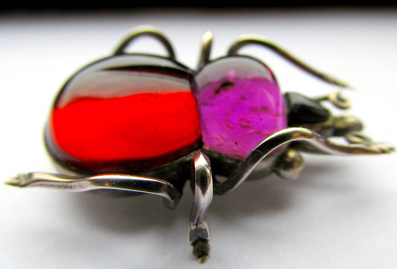 Colorful Victorian rock crystal bug brooch in delightful colors of red and purple set in silver. Fun to wear alone on a lapel or with companions on one's shoulder.
The pin measures 1 5/8