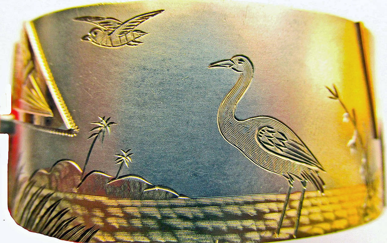 Victorian silver and two-color gold cuff bracelet of Japanesque design depicting a stork standing in water near a house surrounded by flora as a bird flies by. This one of a kind piece will attract attention at work or play. The bracelet's interior