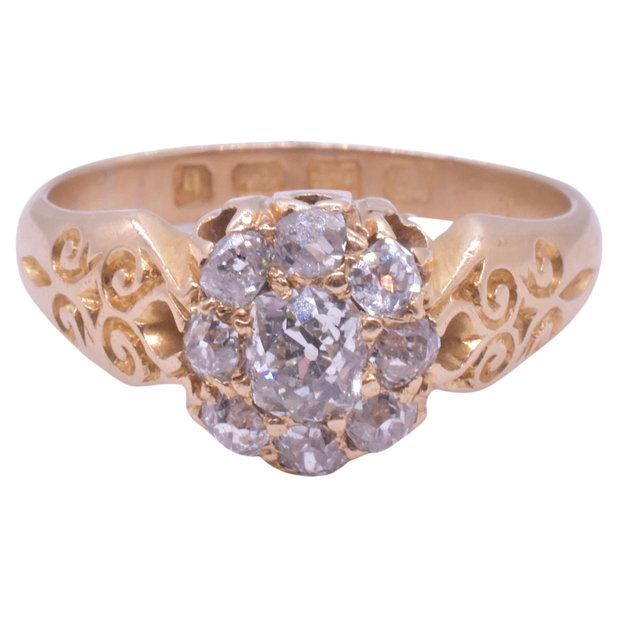Charming 18K Victorian diamond cluster ring with 9 diamonds, hallmarked for Birmingham in the year 1892 with a large center rose cut diamond surrounded by smaller diamonds and hand set with a decorative band of carved flourishes along the shoulders.